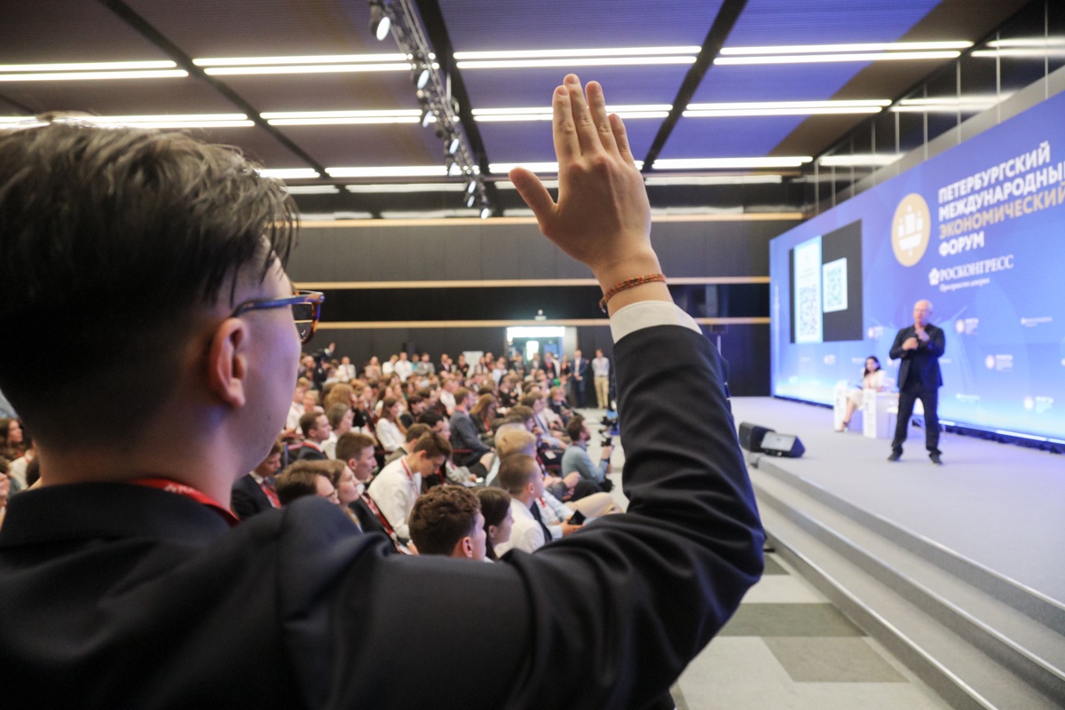 Participant raises a hand in the hall, with a large conference stage ahead.