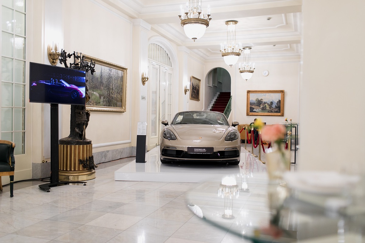 Car stands in a bright reception hall beside a screen and a table with glasses.