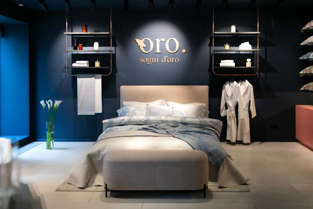 Bed and home textiles are displayed on a dark branded stand.